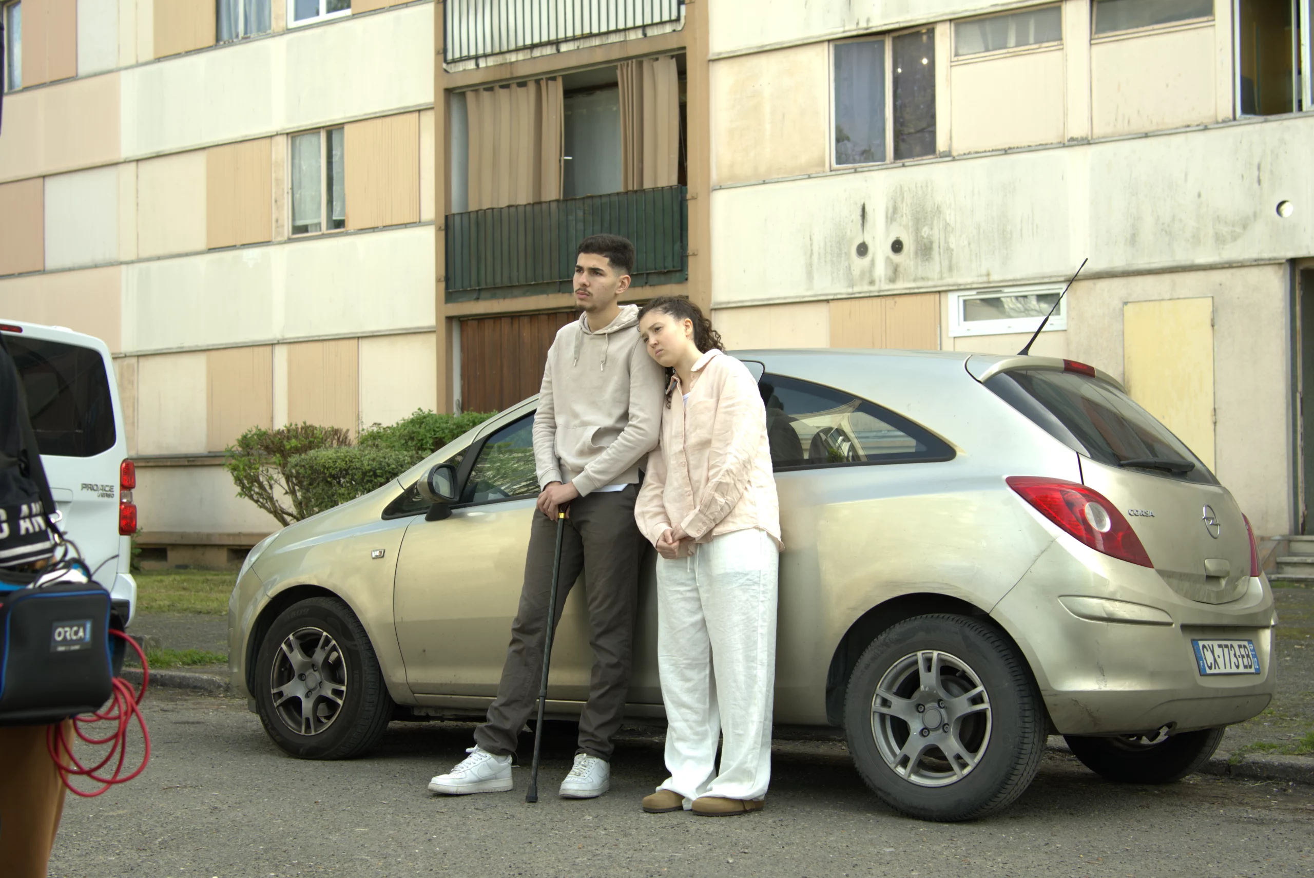 Couple posant devant une voiture dans un quartier résidentiel urbain avec un immeuble en arrière-plan.